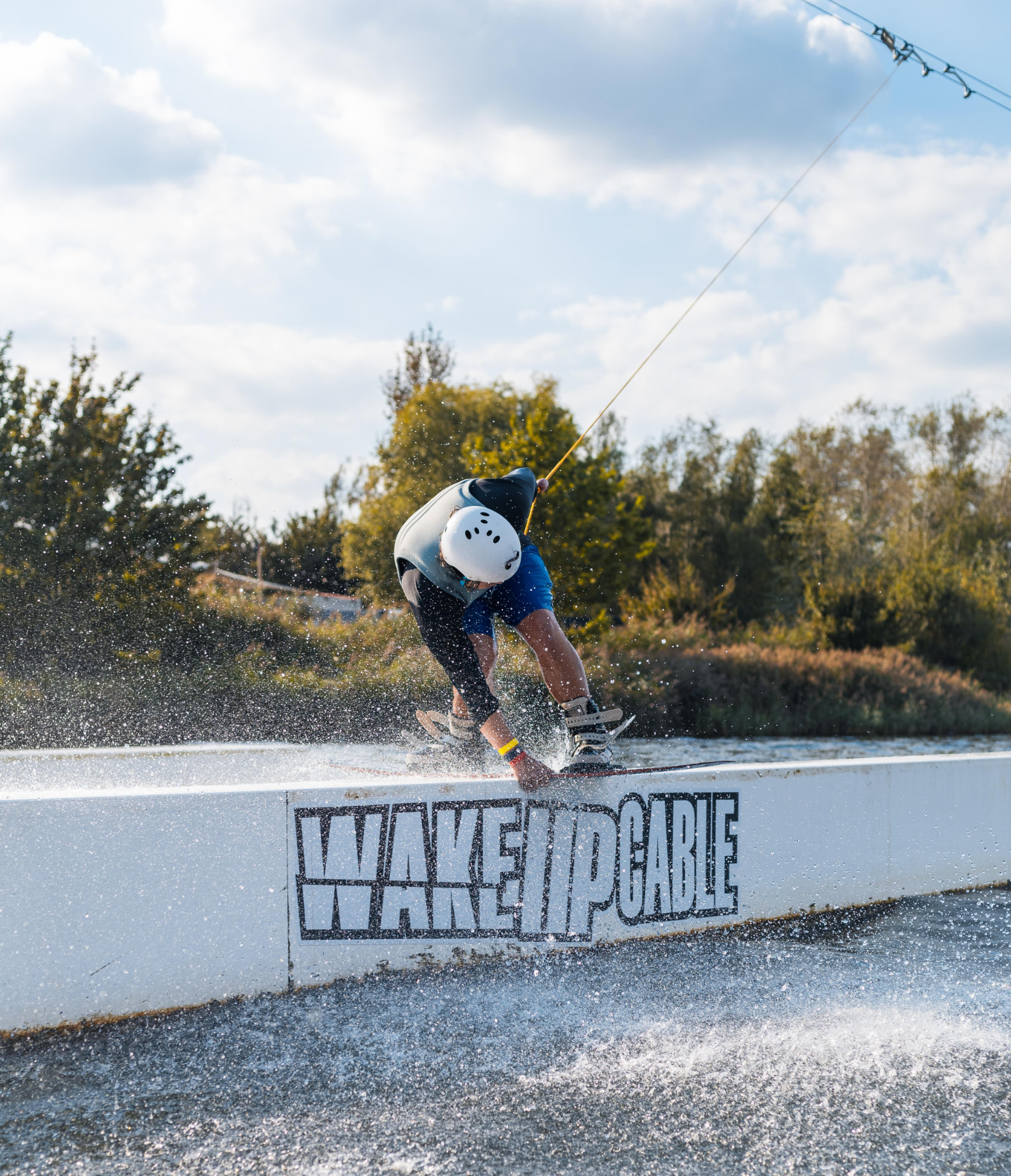 Wakeboarder sliding on a rail at a cable park with Wake Up Cable branding
